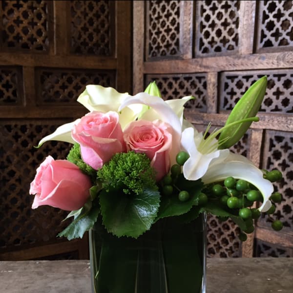 Pink roses and white lilies arranged in a square glass vase