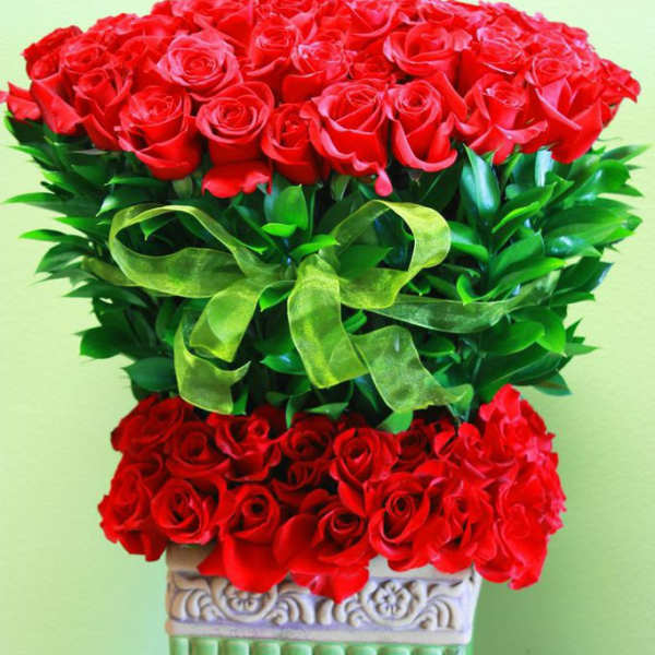 Tall arrangement of red roses with a green ribbon in a decorative pedestal vase
