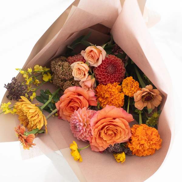 Bouquet of peach, orange, yellow, and pink flowers wrapped in blush paper