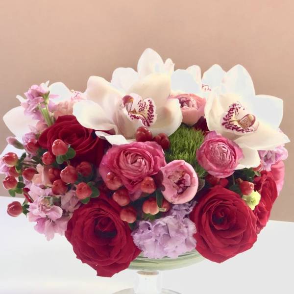 Red and pink bouquet with white orchids in a glass vase