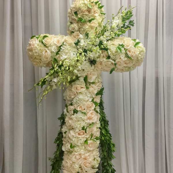 Large floral cross made of white and cream roses with trailing greenery