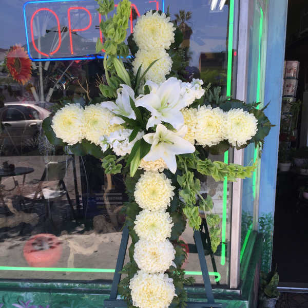 White floral cross arrangement on an easel with lilies and chrysanthemums