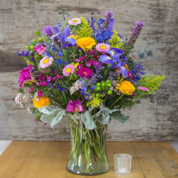 Colorful mixed bouquet in a clear glass vase with a small candle beside it