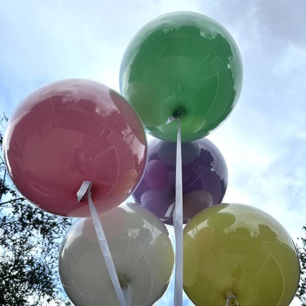 Cluster of colorful balloons with white ribbons against the sky