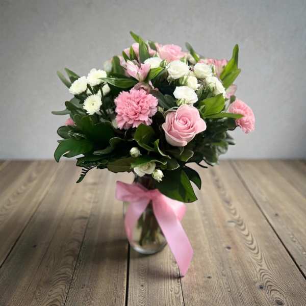 Pink and white bouquet in a glass vase with a pink ribbon