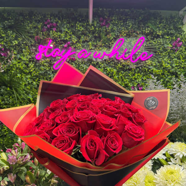 Large bouquet of red roses wrapped in black and red paper held in a flower shop.