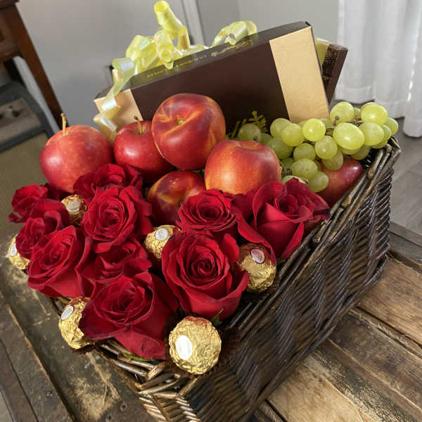 Basket of red roses, apples, grapes, and chocolates with a gift box