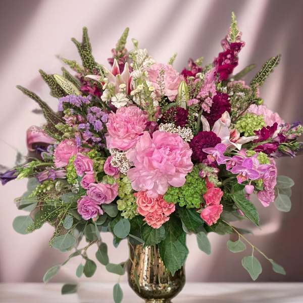 Large pink and purple floral arrangement in a gold vase