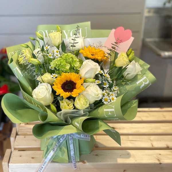 Bouquet of white roses, sunflowers, and small daisies wrapped in green paper