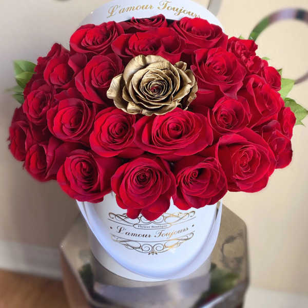 Round box arrangement of red roses with a single gold rose in a white hatbox