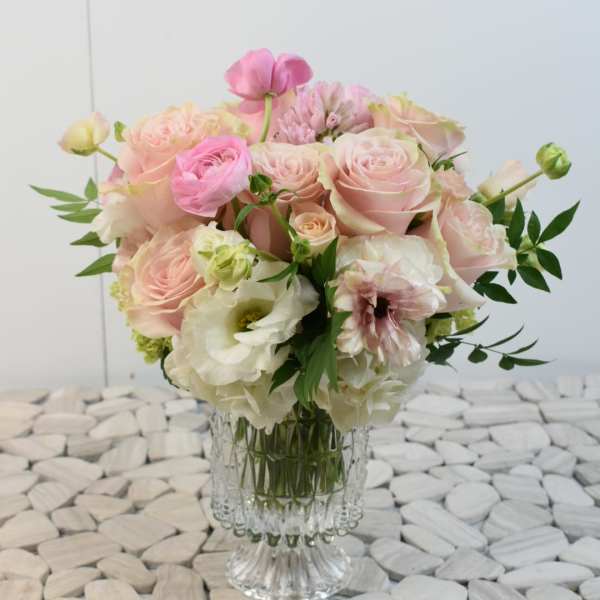 Round arrangement of pale pink and white roses and other blooms in a clear glass vase
