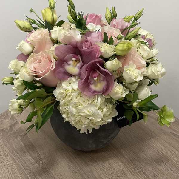 Low round arrangement of pink roses, white hydrangeas, and lavender orchids in a dark bowl vase