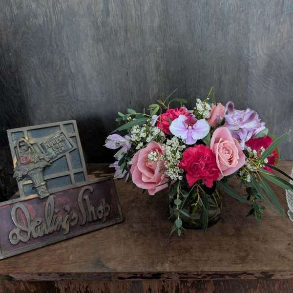 Pink and lavender flower arrangement in a glass vase on a wooden table