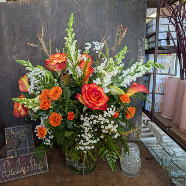 Orange and red roses in a glass vase with white filler flowers