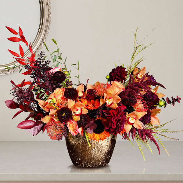 Mixed orange, burgundy, and peach flowers in a textured bronze vase