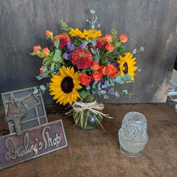 Bouquet of sunflowers, orange roses, and red mums in a glass vase