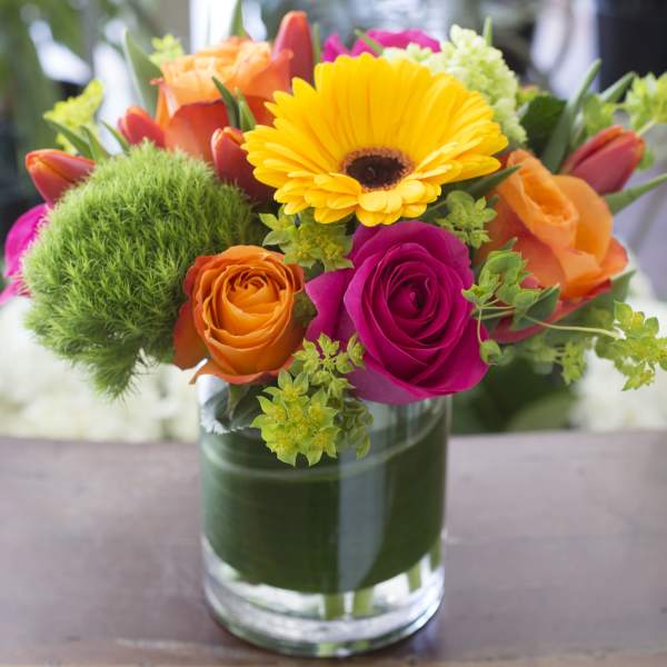 Colorful bouquet of roses and a yellow gerbera daisy in a glass vase