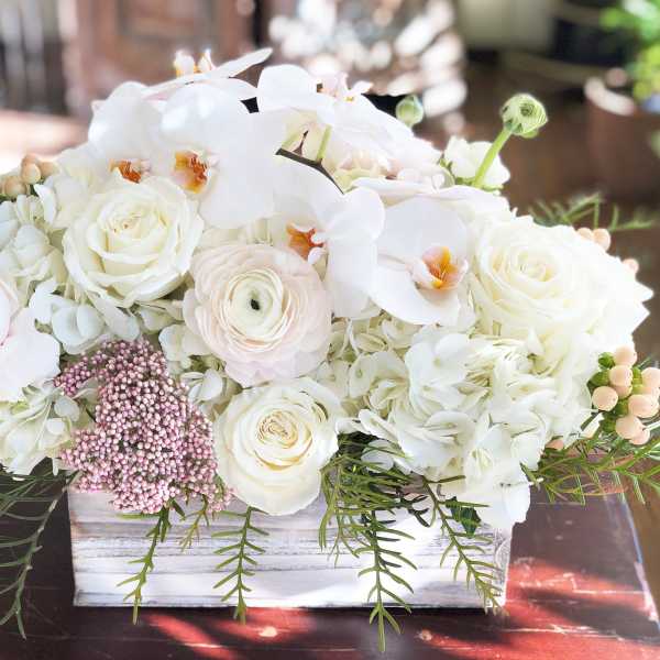 White floral arrangement in a rectangular wooden box with orchids and roses
