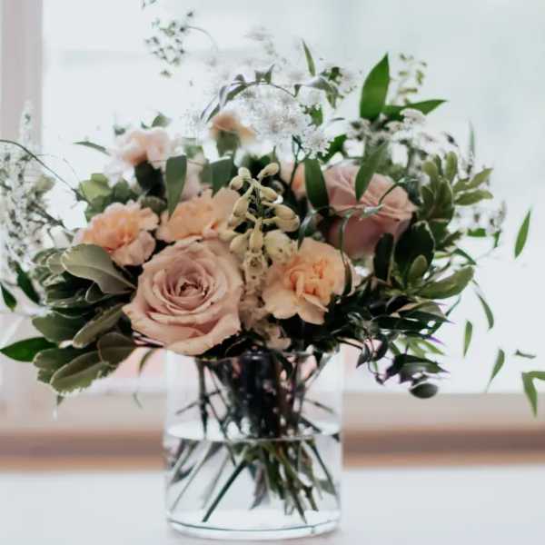 Blush roses and peach carnations in a clear glass vase