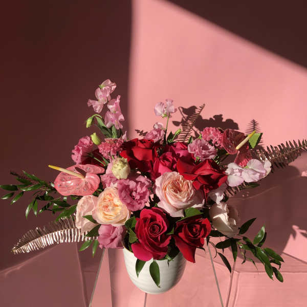 Pink and red rose arrangement in a white vase with tropical accents