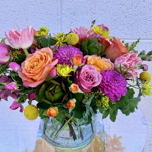 Mixed bouquet of pink, peach, and yellow flowers in a clear glass vase