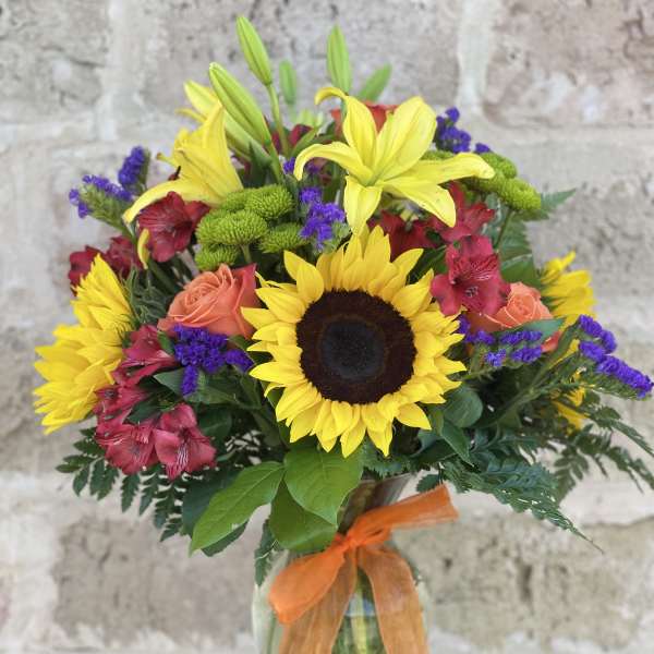 Bright mixed bouquet with sunflowers, lilies, and roses in a glass vase
