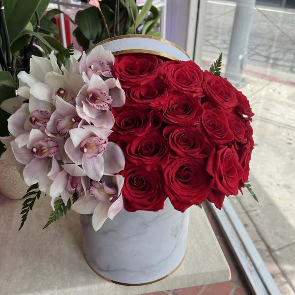 Red roses and pale pink orchids in a white round box