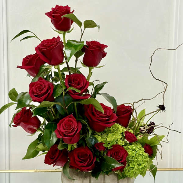 Red roses arranged in a low gray vase with green hydrangeas