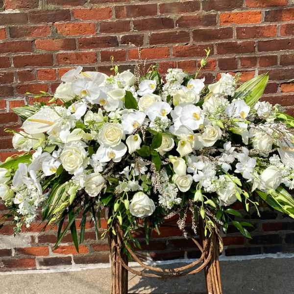 Large white floral arrangement on a stand against a brick wall