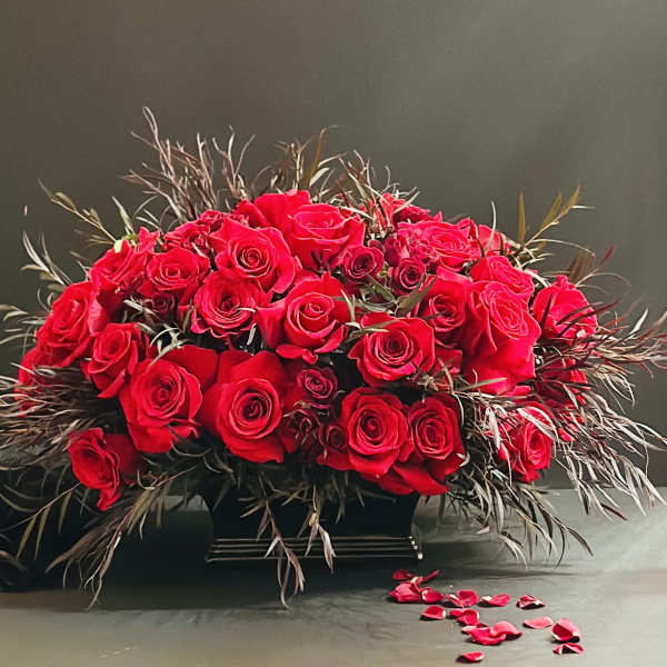 Large arrangement of red roses in a black container with scattered petals