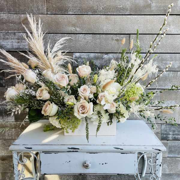 Cream rose arrangement in a white rectangular vase with airy pampas grass