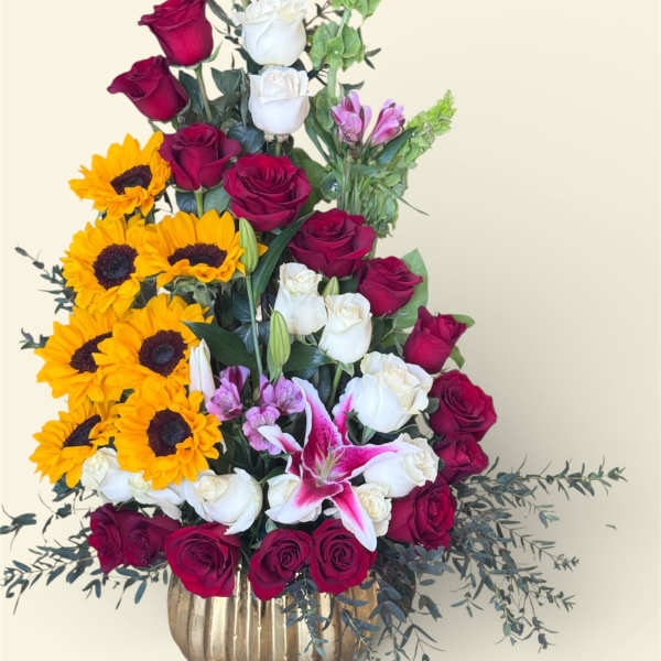 Tall bouquet of red and white roses with sunflowers and lilies in a gold vase
