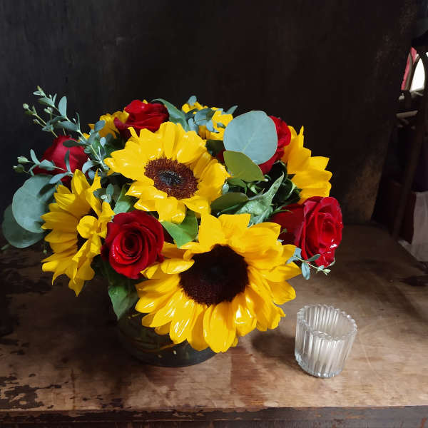 Bouquet of yellow sunflowers and red roses in a dark vase