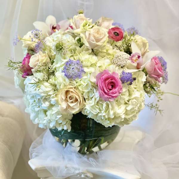 Bouquet of pale hydrangeas, pink roses, and white orchids in a glass vase