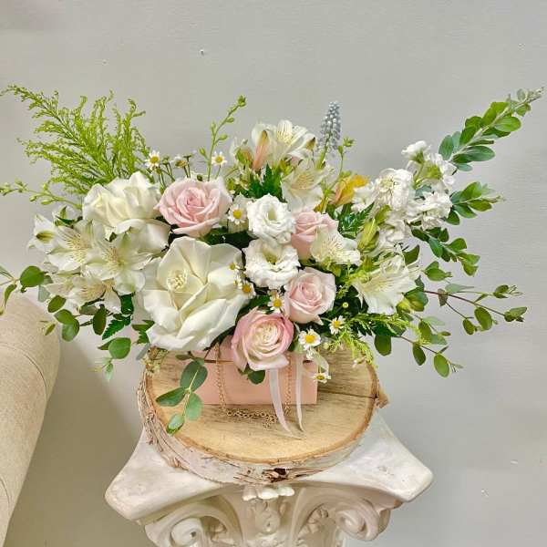 Pink and white floral arrangement in a pink box on a wood slice stand