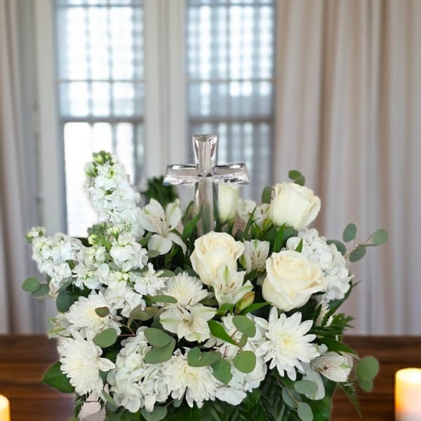 White floral arrangement with roses and a clear cross centerpiece
