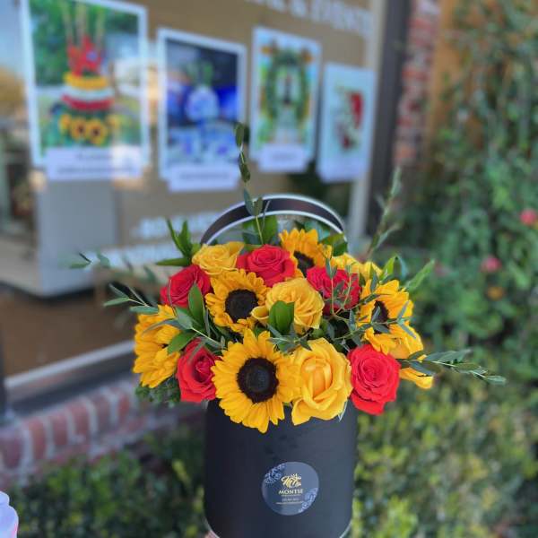 Bouquet of red and yellow roses with sunflowers in a black hat box
