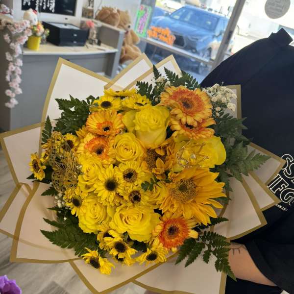 Yellow bouquet of roses and gerbera daisies wrapped in white paper