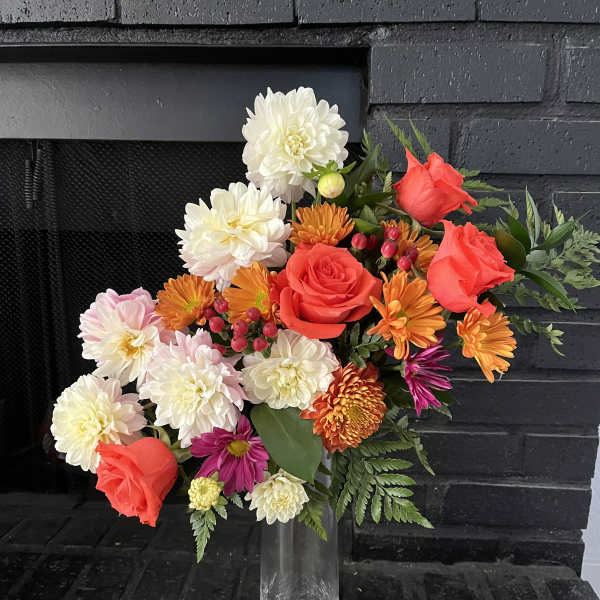 Mixed bouquet of red roses, white dahlias, and orange blooms in a clear vase