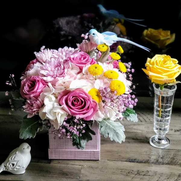Pink and white floral arrangement with yellow accents in a pink box, plus a yellow rose in a vase