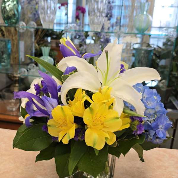 Mixed bouquet of white lilies, yellow alstroemeria, and purple iris in a glass vase