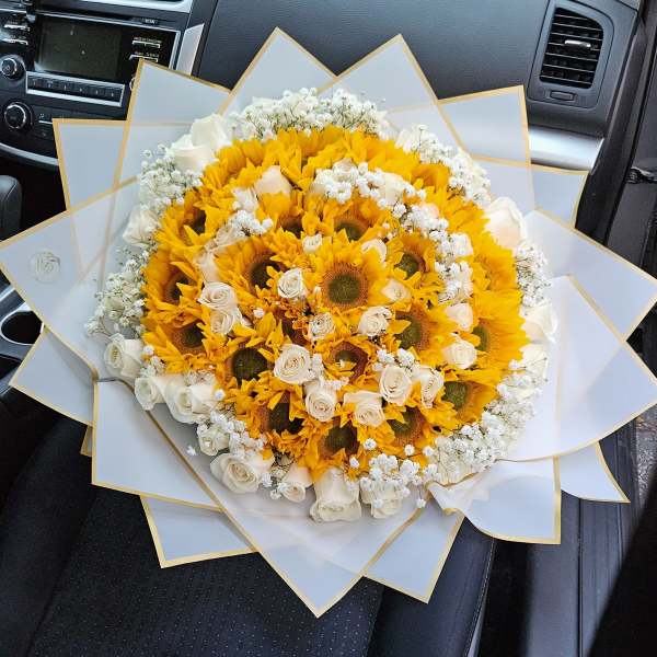 Bouquet of yellow sunflowers and white roses wrapped in white paper