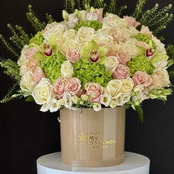 Round bouquet of pale roses and green orchids in a beige hatbox