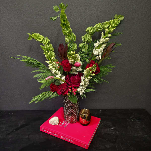 Red roses and white snapdragons in a patterned vase on a pink book