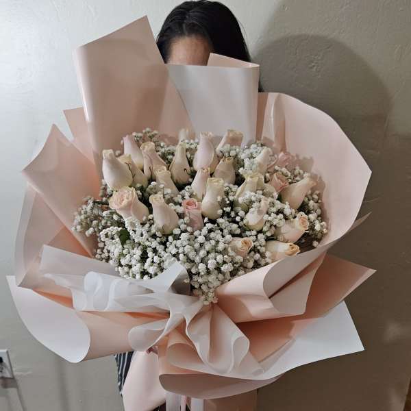 Bouquet of pale pink roses and white baby's breath wrapped in blush paper