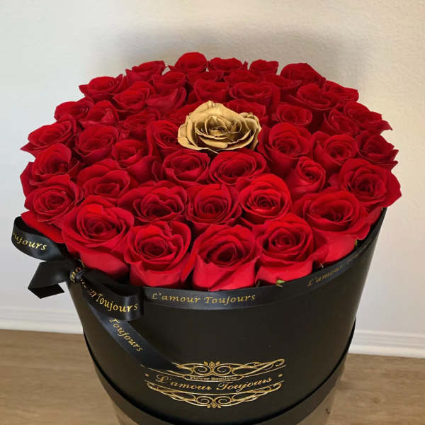 Round bouquet of red roses in a black hatbox with a gold rose at center