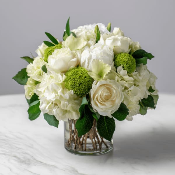 White roses and hydrangeas in a clear glass vase with green accents