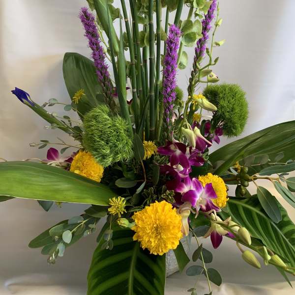 Tall tropical arrangement with purple orchids and yellow blooms in a vase