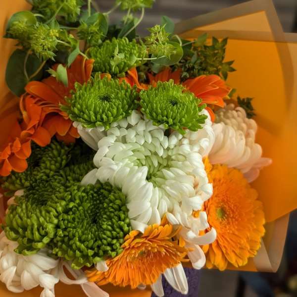 Bouquet of green and white chrysanthemums with bright orange gerbera daisies wrapped in orange paper.
