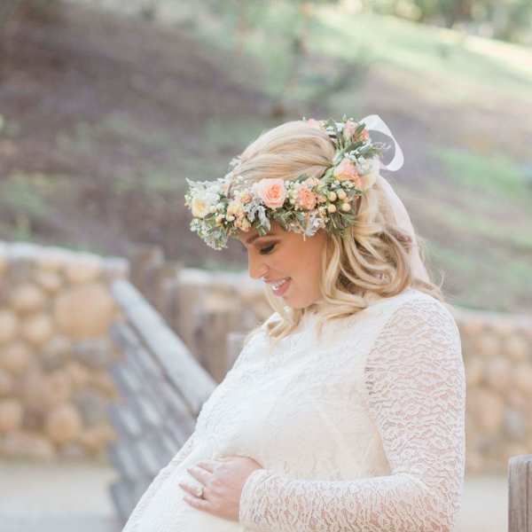 Pregnant woman in a white lace dress wearing a pastel flower crown